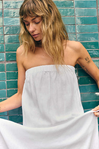 Woman next to tiles wearing a white bandeau style full length beach dress